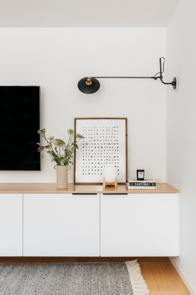 Foto på ett litet minimalistiskt allrum med öppen planlösning, med vita väggar, en väggmonterad TV, ljust trägolv och brunt golv