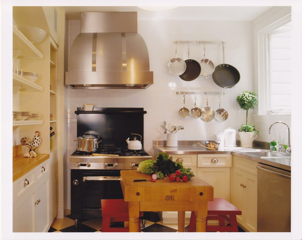 This is an example of an eclectic separate kitchen in San Francisco with a drop-in sink, open cabinets, white cabinets, stainless steel benchtops, white splashback, subway tile splashback and black appliances.
