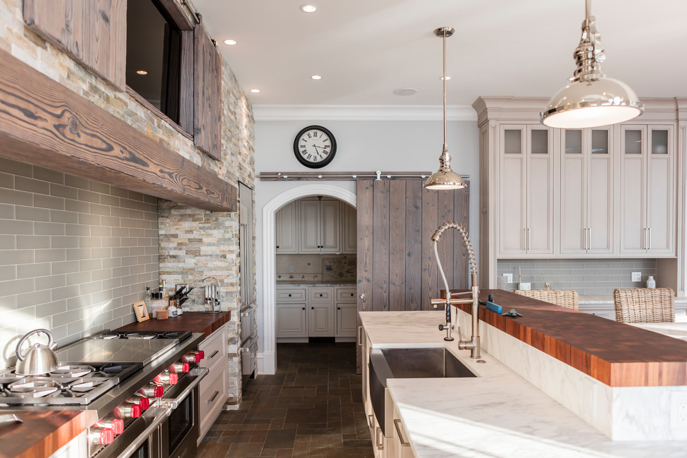 Inspiration for a large beach style single-wall eat-in kitchen in Philadelphia with a farmhouse sink, recessed-panel cabinets, grey cabinets, marble benchtops, grey splashback, glass tile splashback, stainless steel appliances, slate floors and with island.