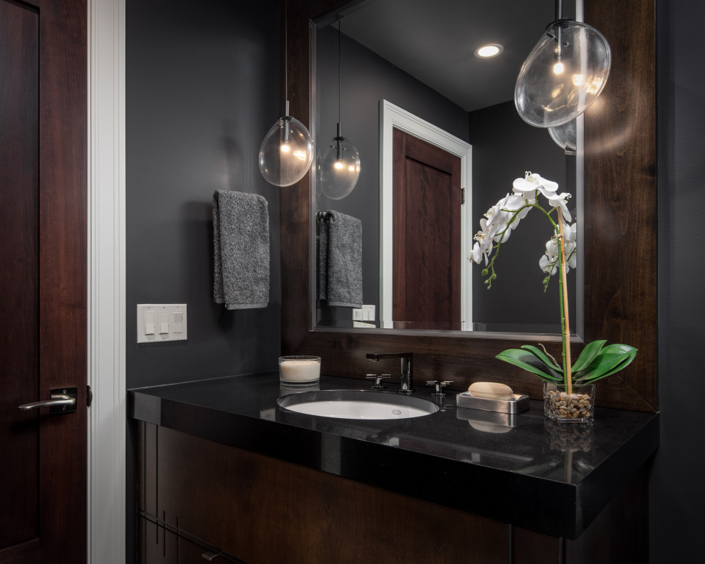 Idée de décoration pour un WC et toilettes design en bois brun de taille moyenne avec un placard à porte plane, un mur gris, un lavabo encastré, un plan de toilette en granite, un plan de toilette noir et meuble-lavabo encastré.