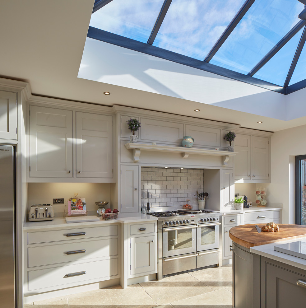 This is an example of a large traditional single-wall eat-in kitchen in Wiltshire with a farmhouse sink, recessed-panel cabinets, grey cabinets, quartz benchtops, beige splashback, stone slab splashback, stainless steel appliances, limestone floors and a peninsula.
