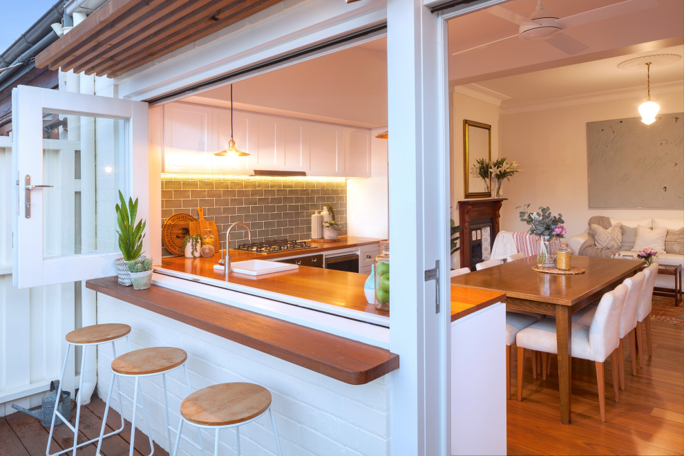 Design ideas for a traditional l-shaped open plan kitchen in Sydney with a drop-in sink, shaker cabinets, white cabinets, wood benchtops, grey splashback, subway tile splashback, stainless steel appliances, medium hardwood floors, no island, brown floor and brown benchtop.