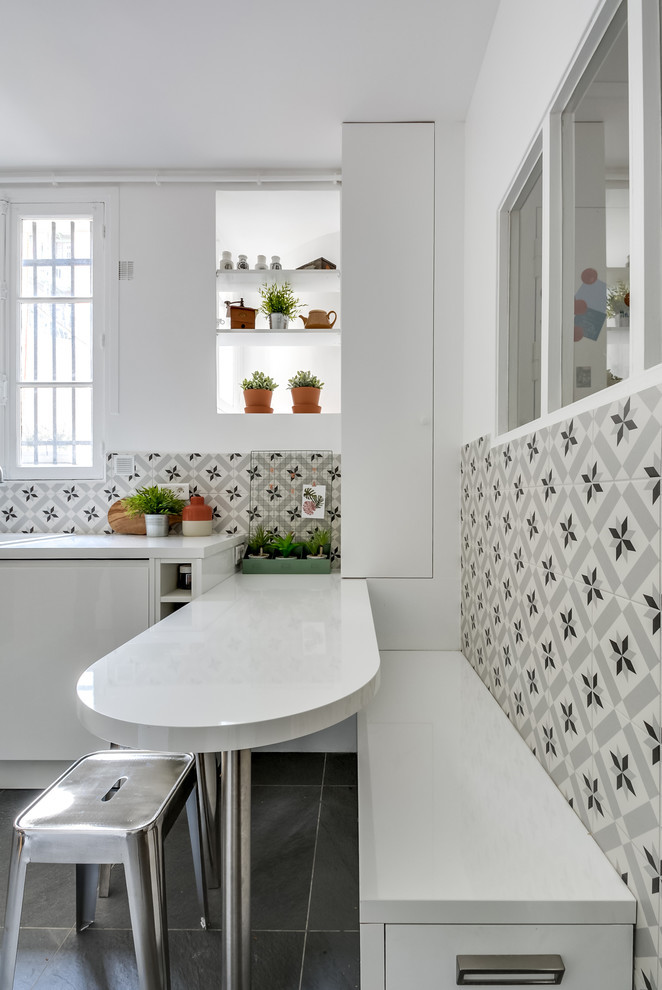Mid-sized contemporary l-shaped eat-in kitchen in Montpellier with beaded inset cabinets, white cabinets, with island, laminate benchtops, cement tile splashback, porcelain floors, grey floor, white benchtop, a drop-in sink, multi-coloured splashback and stainless steel appliances.