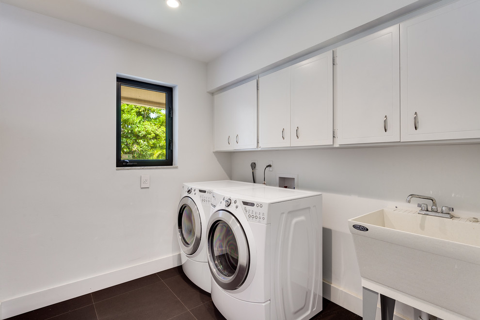 Photo of a mid-sized contemporary single-wall dedicated laundry room in Miami with an utility sink, shaker cabinets, white cabinets, white walls, concrete floors, a side-by-side washer and dryer and grey floor.