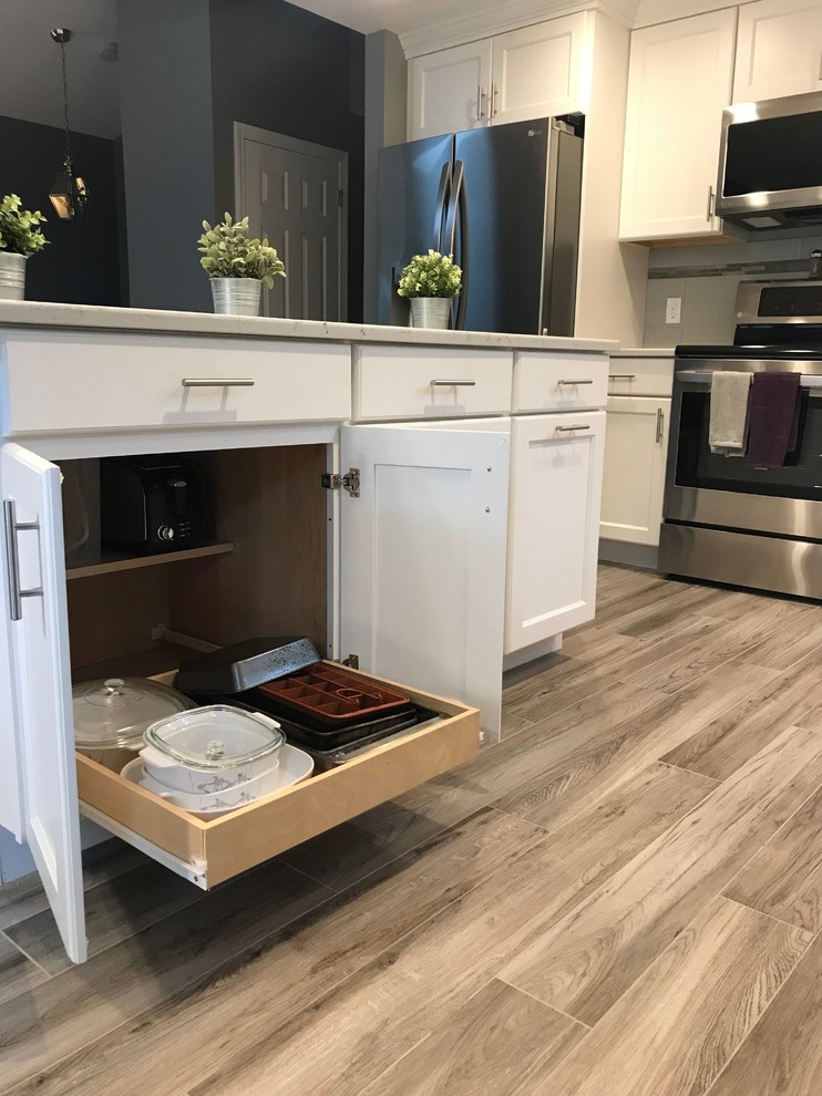 Inspiration for a mid-sized transitional l-shaped porcelain tile and gray floor open concept kitchen remodel in Boston with a single-bowl sink, flat-panel cabinets, white cabinets, quartz countertops, gray backsplash, subway tile backsplash, stainless steel appliances, an island and white countertops