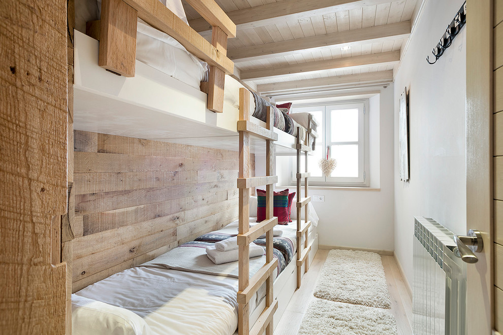 This is an example of a mid-sized country gender-neutral kids' bedroom for kids 4-10 years old in Barcelona with white walls and light hardwood floors.