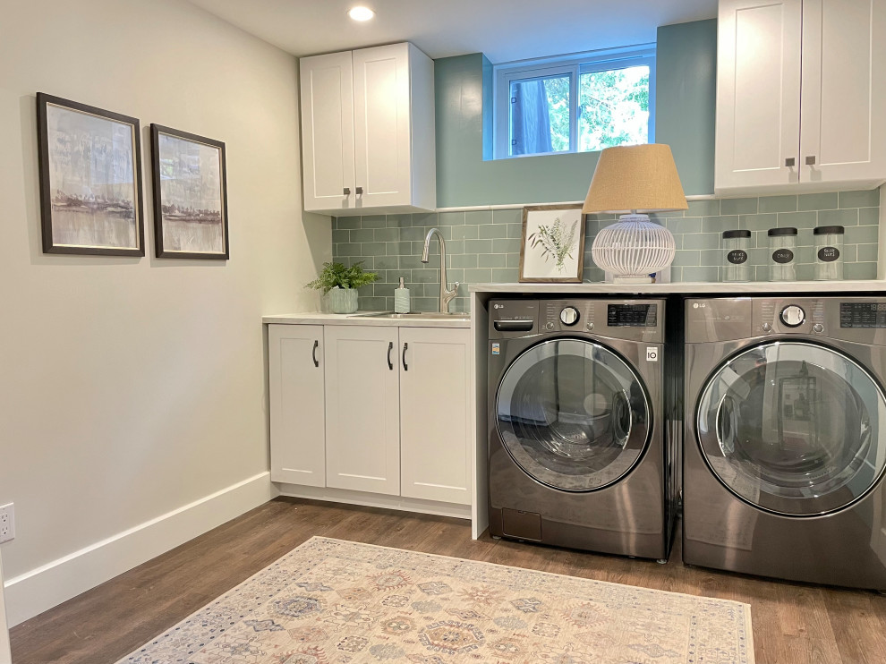 Idéer för att renovera en mellanstor vintage vita vitt tvättstuga enbart för tvätt, med en nedsänkt diskho, skåp i shakerstil, vita skåp, laminatbänkskiva, grönt stänkskydd, stänkskydd i porslinskakel, beige väggar, vinylgolv, en tvättmaskin och torktumlare bredvid varandra och brunt golv