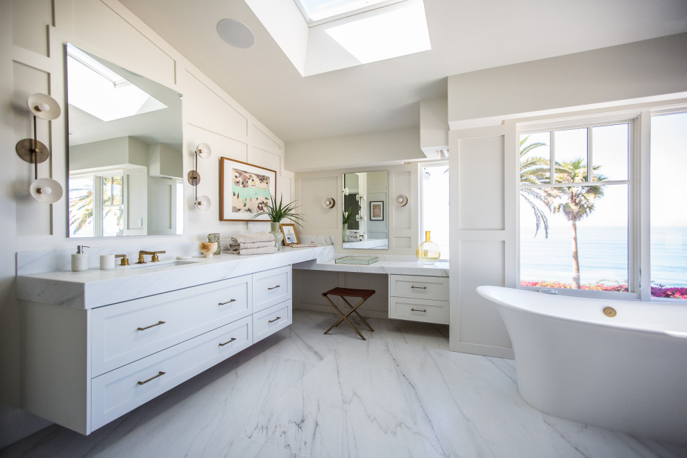 Photo of a beach style master bathroom in San Diego with shaker cabinets, white cabinets, a freestanding tub, white walls, an undermount sink, white floor, white benchtops, vaulted, panelled walls, a single vanity and a floating vanity.