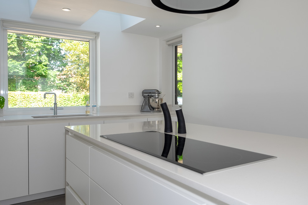 This is an example of a mid-sized industrial l-shaped open plan kitchen in Hampshire with an undermount sink, flat-panel cabinets, white cabinets, quartzite benchtops, white splashback, stainless steel appliances, linoleum floors, with island, multi-coloured floor and white benchtop.