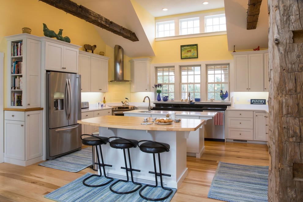 Photo of a large country u-shaped eat-in kitchen in Boston with a farmhouse sink, flat-panel cabinets, white cabinets, quartz benchtops, stainless steel appliances, light hardwood floors and multiple islands.