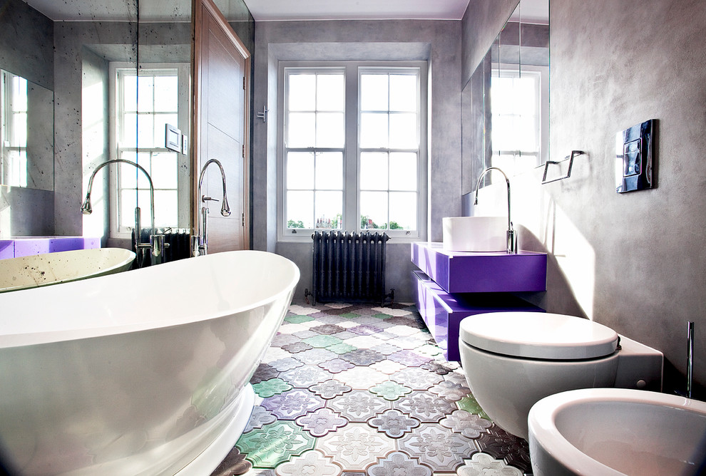 Design ideas for a contemporary bathroom in London with a vessel sink, flat-panel cabinets, a freestanding tub, a wall-mount toilet, grey walls and multi-coloured floor.