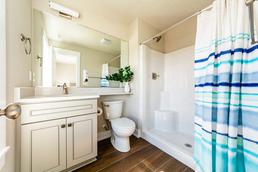 This is an example of a small beach style 3/4 bathroom in Other with beaded inset cabinets, grey cabinets, an alcove shower, a two-piece toilet, beige walls, medium hardwood floors, an undermount sink, quartzite benchtops, brown floor, a shower curtain and grey benchtops.