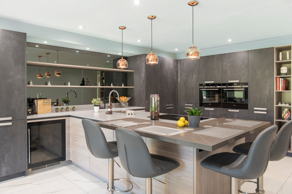 This is an example of a contemporary u-shaped open plan kitchen in Buckinghamshire with flat-panel cabinets, grey cabinets, quartzite benchtops, an undermount sink, mirror splashback, a peninsula, beige floor and grey benchtop.