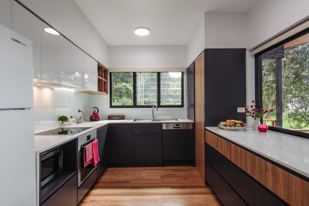 Small contemporary u-shaped kitchen in Brisbane with dark wood cabinets, white splashback, stainless steel appliances, medium hardwood floors, no island and flat-panel cabinets.