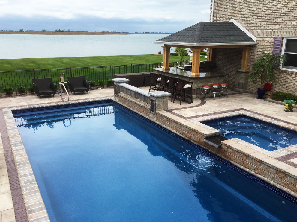 Mediterranean backyard custom-shaped pool in Detroit with a hot tub and brick pavers.