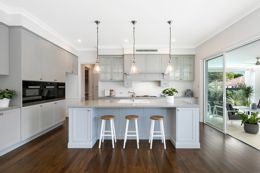 Design ideas for a large contemporary galley eat-in kitchen in Sydney with a farmhouse sink, shaker cabinets, grey cabinets, white splashback, subway tile splashback, stainless steel appliances, dark hardwood floors, multiple islands and grey benchtop.