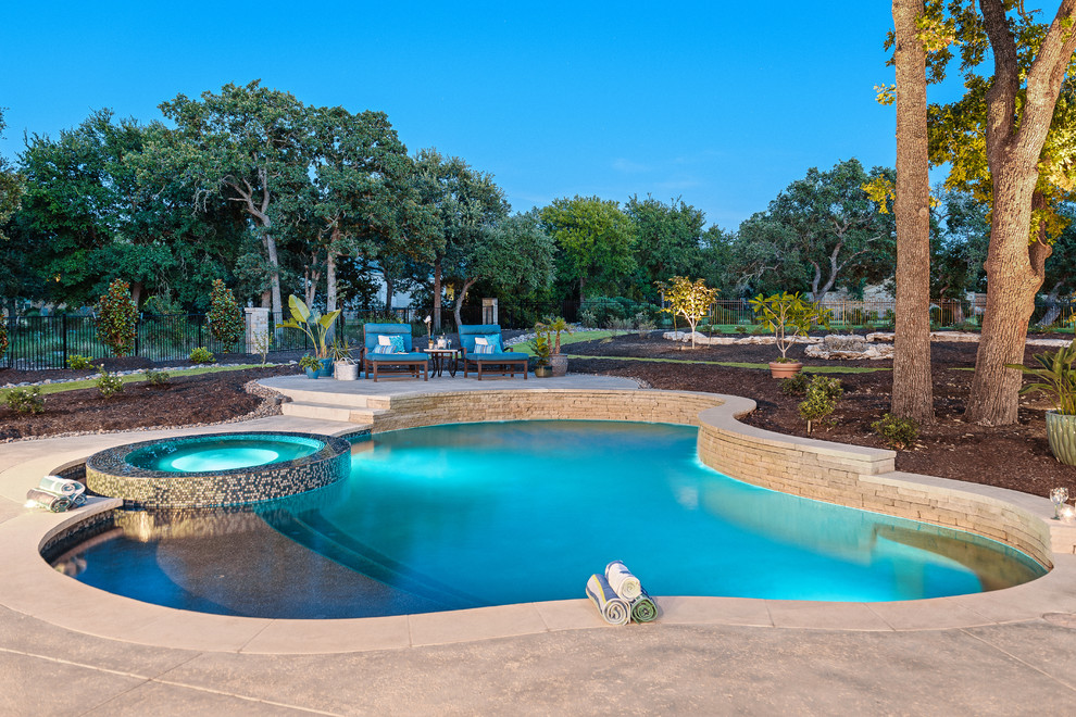 This is an example of a mid-sized contemporary backyard custom-shaped natural pool in Austin with a hot tub and stamped concrete.