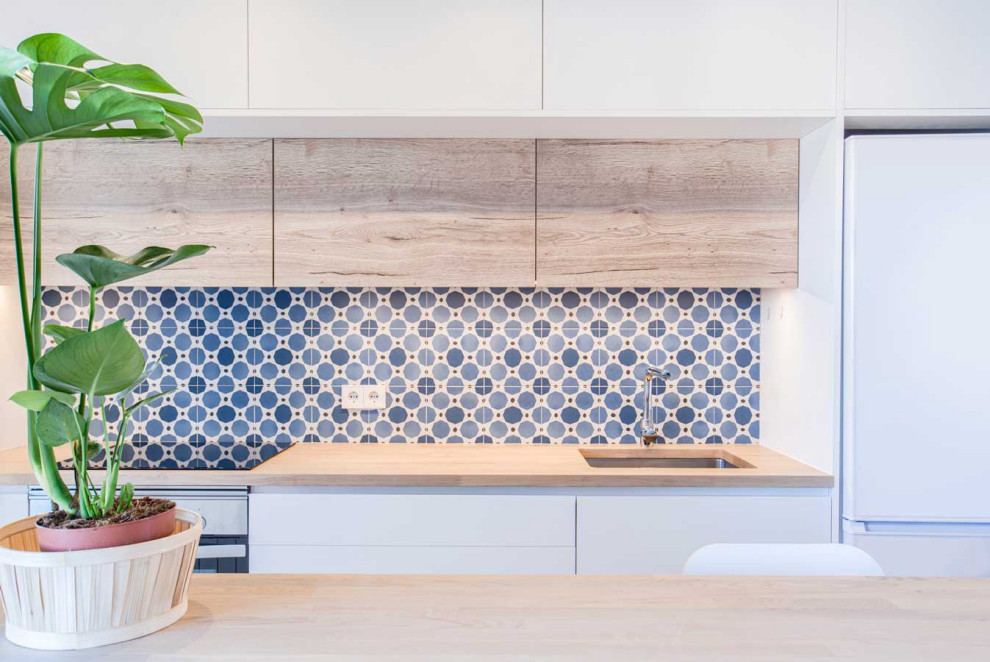 This is an example of a mid-sized modern open plan kitchen in Barcelona with an undermount sink, flat-panel cabinets, medium wood cabinets, wood benchtops, blue splashback, ceramic splashback, white appliances, porcelain floors, with island, beige floor and beige benchtop.