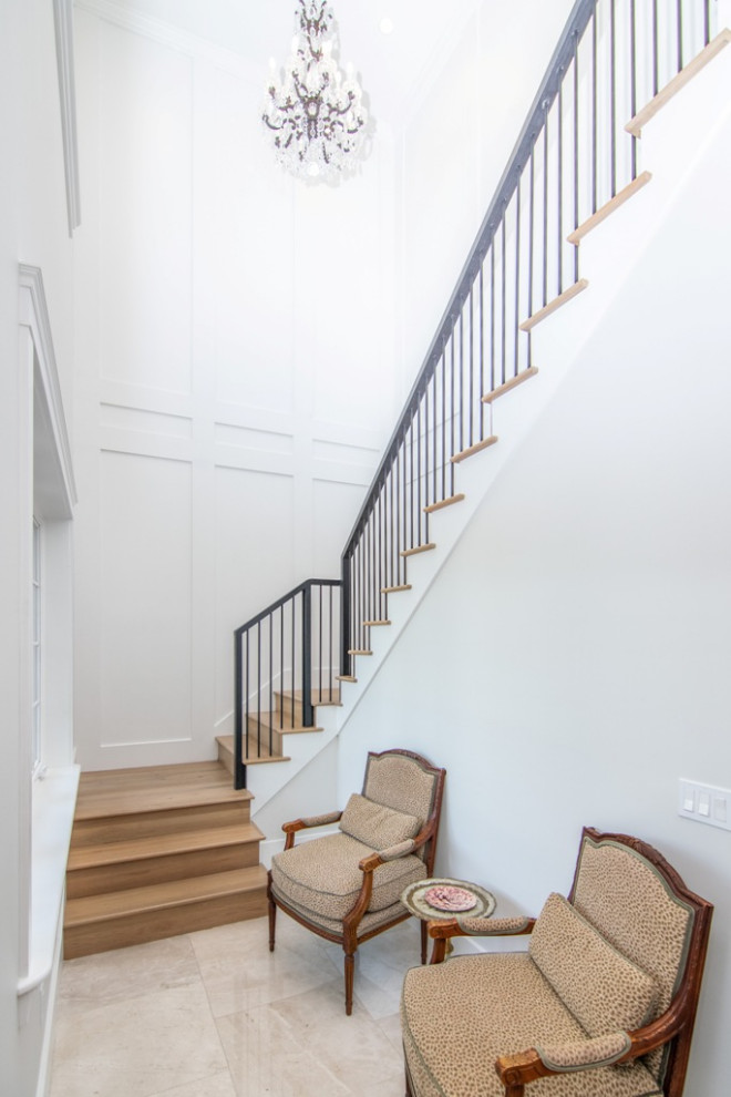 Imagen de escalera recta clásica renovada grande con escalones de madera, contrahuellas de madera, barandilla de metal y boiserie