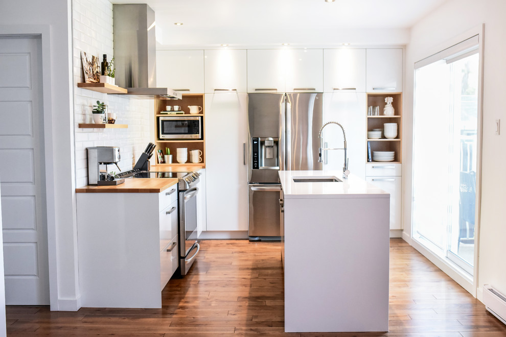 Photo of a small scandinavian l-shaped separate kitchen in Montreal with an undermount sink, flat-panel cabinets, white cabinets, quartzite benchtops, white splashback, ceramic splashback, stainless steel appliances, medium hardwood floors, with island and orange floor.