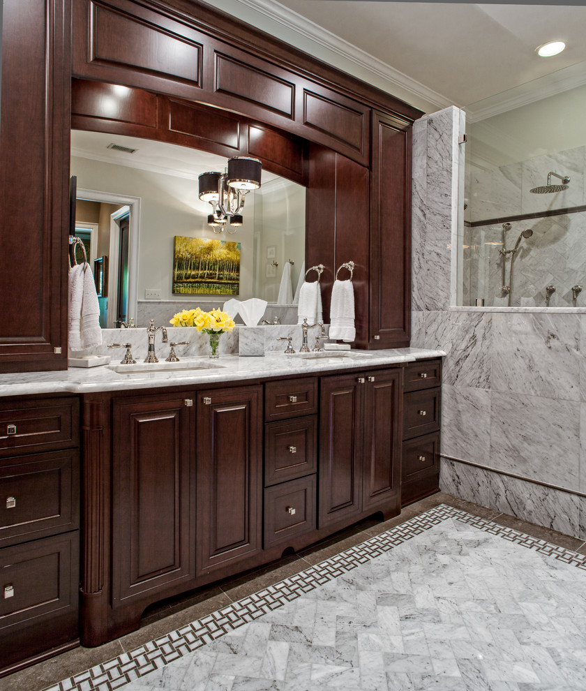 Mid-sized traditional master bathroom in Charlotte with an undermount sink, dark wood cabinets, marble benchtops, a freestanding tub, a curbless shower, a two-piece toilet, gray tile, stone tile, grey walls, limestone floors and raised-panel cabinets.