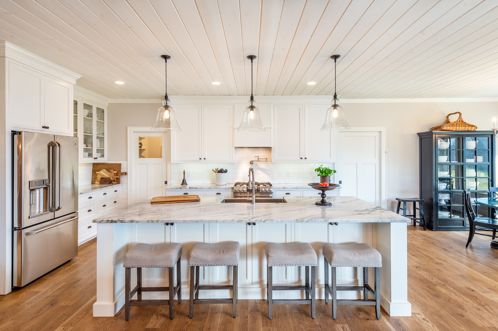 Inspiration for a traditional l-shaped kitchen in Other with a farmhouse sink, shaker cabinets, white cabinets, white splashback, subway tile splashback, stainless steel appliances, medium hardwood floors, with island, brown floor and grey benchtop.