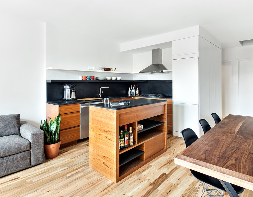 Photo of a small scandinavian l-shaped open plan kitchen in New York with flat-panel cabinets, black splashback, stainless steel appliances, light hardwood floors and with island.