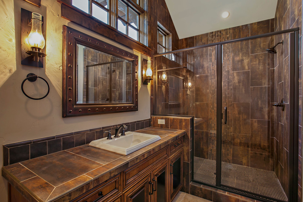 Photo of a country bathroom in Other with a drop-in sink, raised-panel cabinets, dark wood cabinets, tile benchtops, an alcove shower, brown tile, brown walls and brown benchtops.