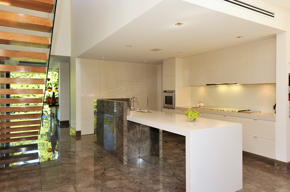 This is an example of a traditional l-shaped open plan kitchen in Melbourne with an undermount sink, marble benchtops, white splashback, glass sheet splashback, stainless steel appliances, marble floors, with island and grey floor.