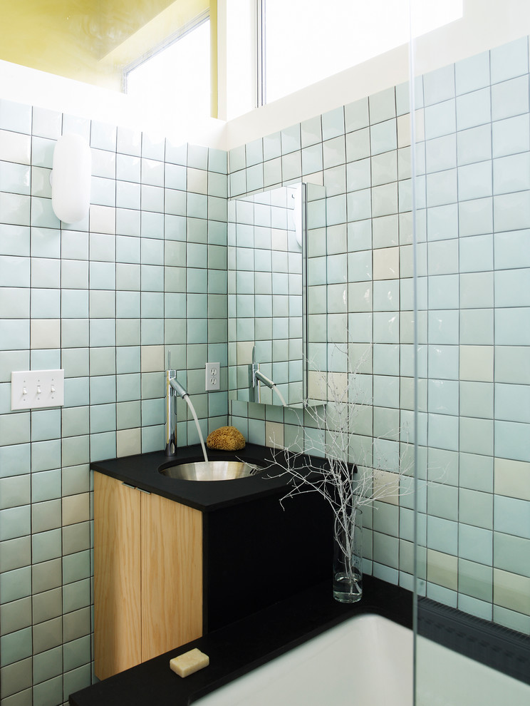 Photo of a small industrial bathroom in Seattle with an undermount sink, flat-panel cabinets, medium wood cabinets, solid surface benchtops, an undermount tub, blue tile and ceramic tile.