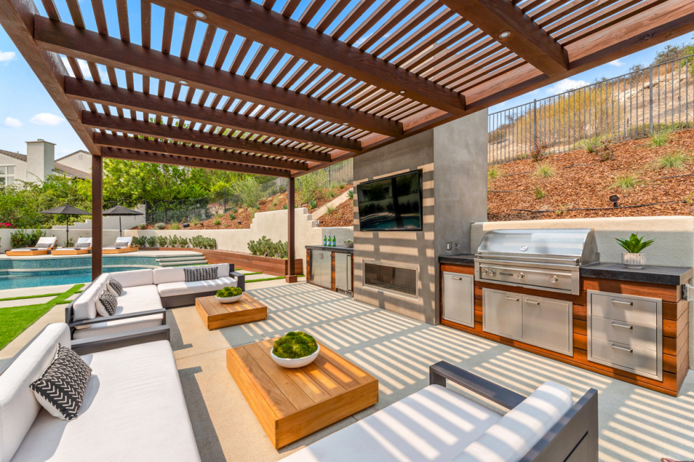 This is an example of a large contemporary backyard patio in Los Angeles with an outdoor kitchen, concrete pavers and a pergola.