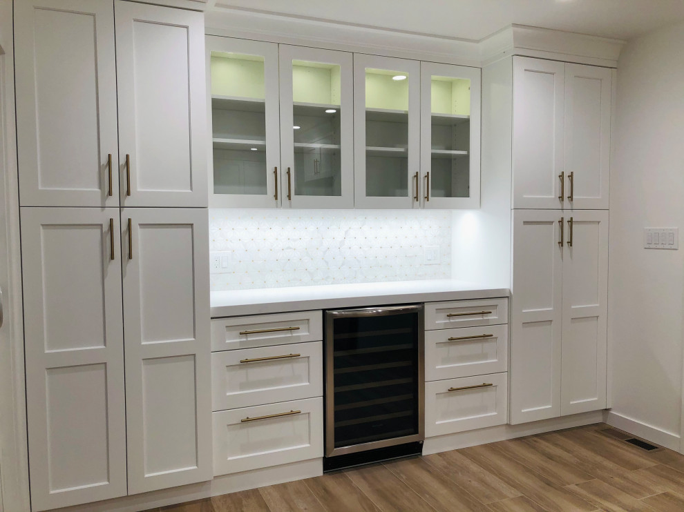 Mid-sized transitional l-shaped eat-in kitchen in San Francisco with a farmhouse sink, recessed-panel cabinets, white cabinets, quartz benchtops, white splashback, mosaic tile splashback, stainless steel appliances, medium hardwood floors, a peninsula, brown floor and white benchtop.