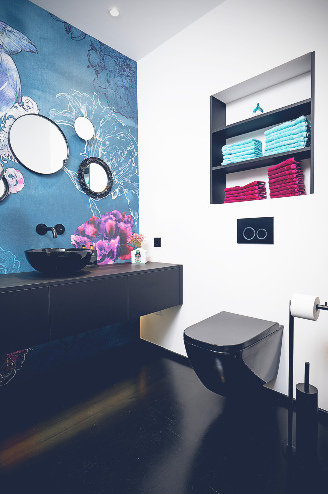 Mittelgroße Gästetoilette mit schwarzen Schränken, blauer Wandfarbe, Aufsatzwaschbecken, Waschtisch aus Holz, schwarzem Boden, schwebendem Waschtisch und Tapetenwänden in Düsseldorf