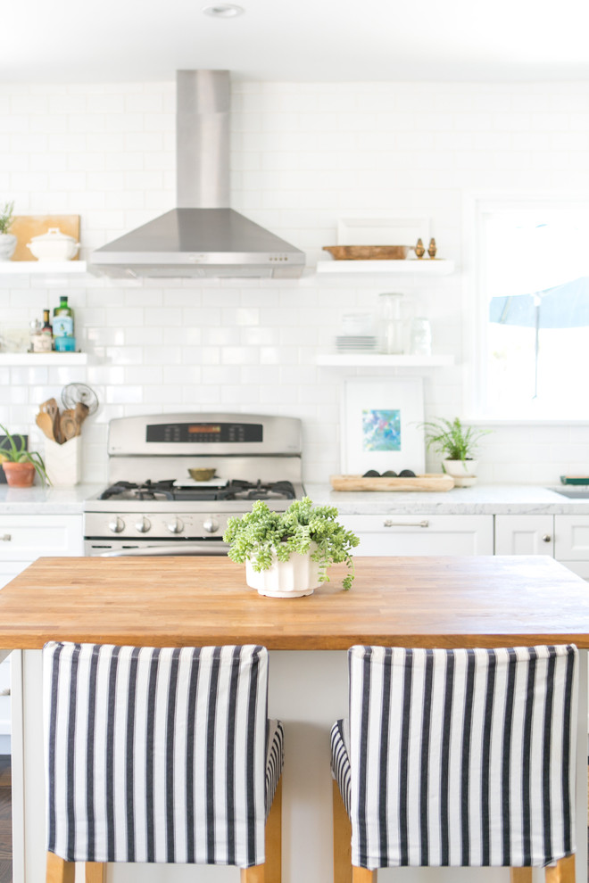 Photo of a beach style kitchen in Los Angeles with a single-bowl sink, shaker cabinets, white cabinets, marble benchtops, white splashback, subway tile splashback, panelled appliances and dark hardwood floors.