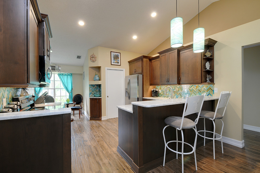 Mid-sized tropical u-shaped eat-in kitchen in Tampa with an undermount sink, shaker cabinets, medium wood cabinets, granite benchtops, brown splashback, glass tile splashback, stainless steel appliances, porcelain floors and a peninsula.