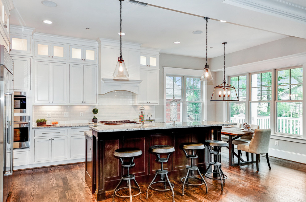 Example of a mid-sized transitional l-shaped medium tone wood floor and brown floor open concept kitchen design in DC Metro with granite countertops, stainless steel appliances, an island, shaker cabinets, white cabinets, white backsplash and subway tile backsplash
