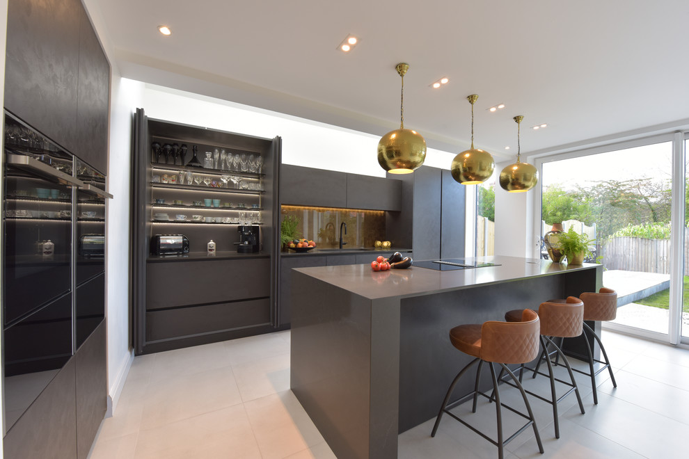 Mid-sized contemporary open plan kitchen in Manchester with an undermount sink, flat-panel cabinets, grey cabinets, quartzite benchtops, metallic splashback, glass sheet splashback, black appliances, porcelain floors, with island, white floor and grey benchtop.