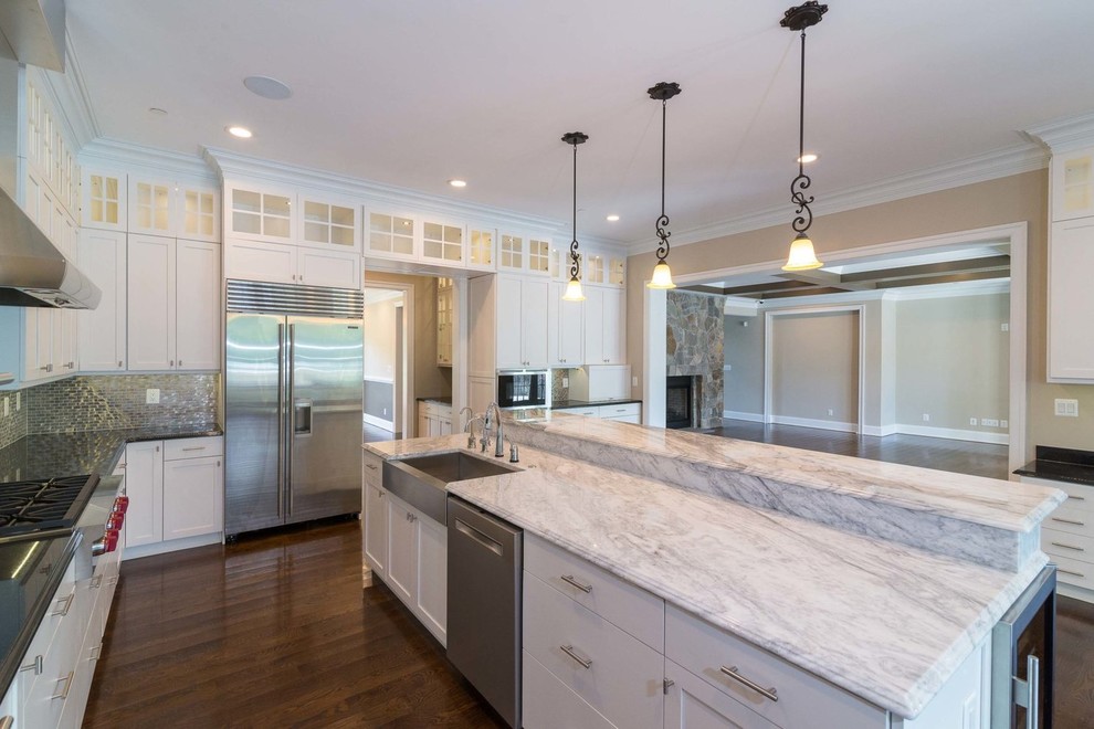 This is an example of a large traditional l-shaped open plan kitchen in DC Metro with a farmhouse sink, shaker cabinets, white cabinets, marble benchtops, metallic splashback, mosaic tile splashback, stainless steel appliances, dark hardwood floors, with island and brown floor.