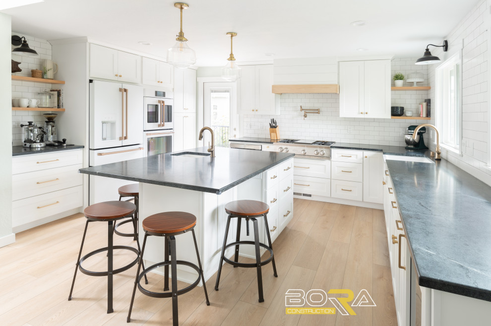 Inspiration for a mid-sized transitional u-shaped medium tone wood floor and brown floor eat-in kitchen remodel in Seattle with shaker cabinets, white cabinets, quartz countertops, white backsplash, ceramic backsplash, stainless steel appliances, an island and black countertops