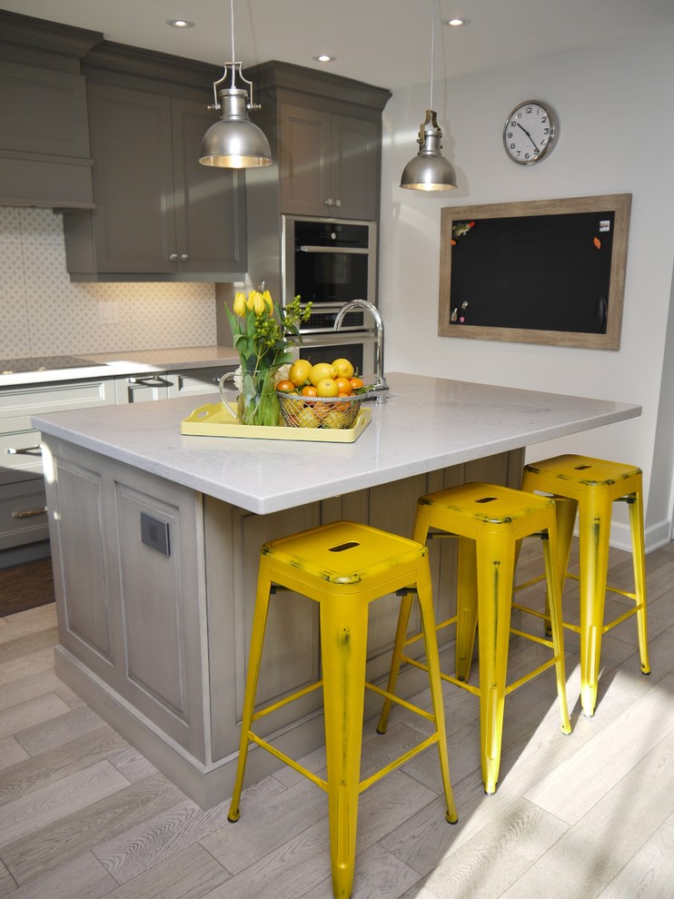 Mid-sized transitional l-shaped light wood floor enclosed kitchen photo in Toronto with an undermount sink, recessed-panel cabinets, gray cabinets, quartz countertops, white backsplash, porcelain backsplash, stainless steel appliances and an island