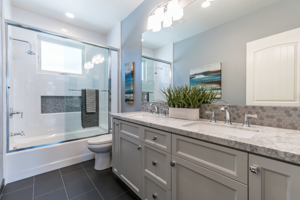 Inspiration for a mid-sized transitional bathroom in San Francisco with grey cabinets, an alcove tub, a shower/bathtub combo, grey walls, an undermount sink, black floor, a sliding shower screen, grey benchtops, recessed-panel cabinets, a two-piece toilet, white tile, subway tile, porcelain floors and marble benchtops.