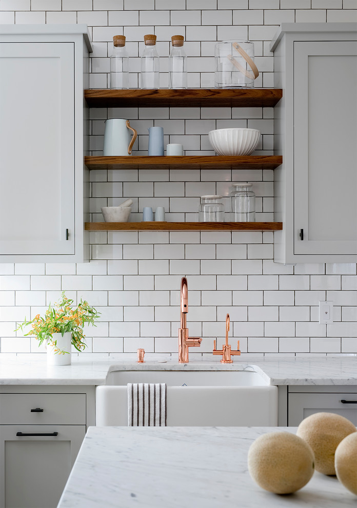 Large transitional u-shaped medium tone wood floor enclosed kitchen photo in New York with a farmhouse sink, shaker cabinets, white cabinets, quartzite countertops, white backsplash, subway tile backsplash, stainless steel appliances and an island
