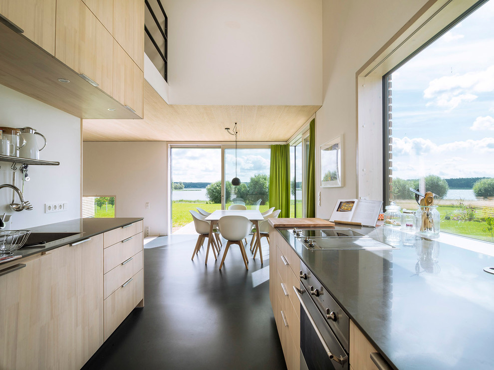 This is an example of a large contemporary galley eat-in kitchen in Hamburg with flat-panel cabinets, light wood cabinets, stainless steel appliances, a drop-in sink, white splashback, no island, concrete floors and black floor.