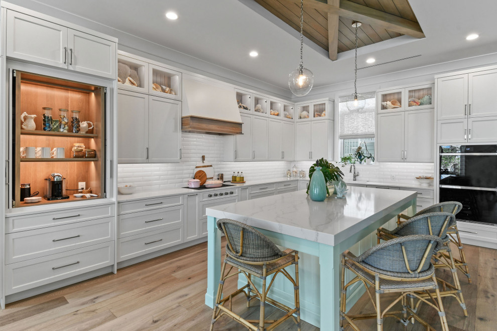 Design ideas for a medium sized nautical l-shaped kitchen in Other with white cabinets, engineered stone countertops, white splashback, metro tiled splashback, integrated appliances, light hardwood flooring, an island, brown floors, white worktops and a drop ceiling.