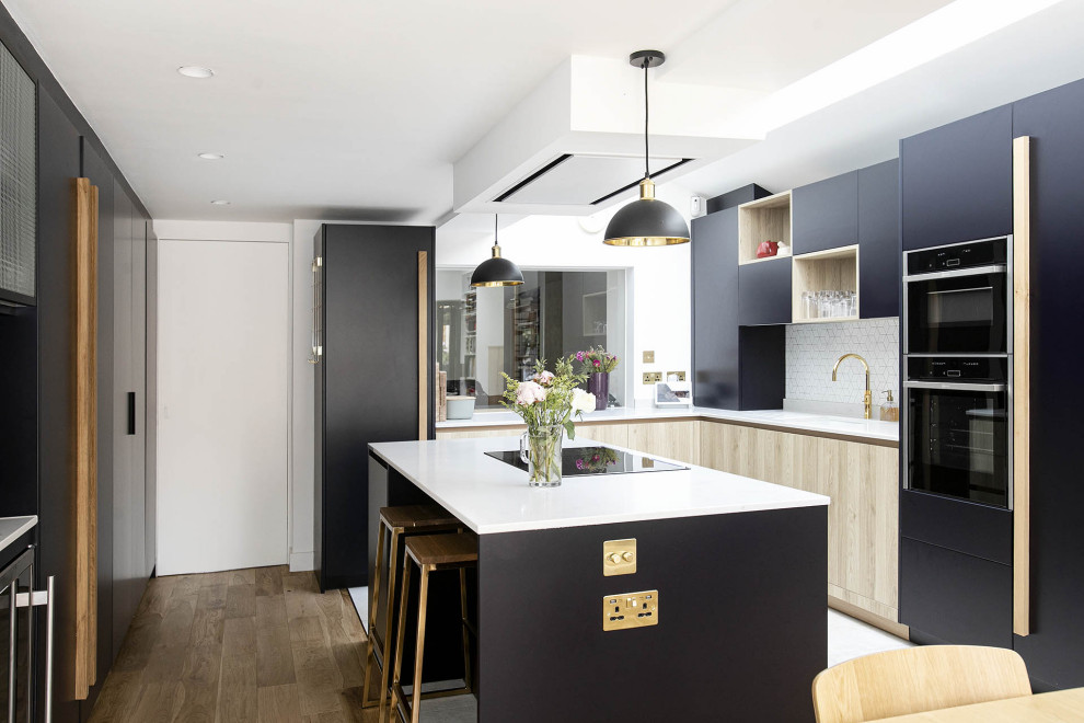 This is an example of a small contemporary l-shaped open plan kitchen in London with an undermount sink, beaded inset cabinets, black cabinets, quartzite benchtops, white splashback, ceramic splashback, black appliances, ceramic floors, with island, multi-coloured floor, white benchtop and vaulted.