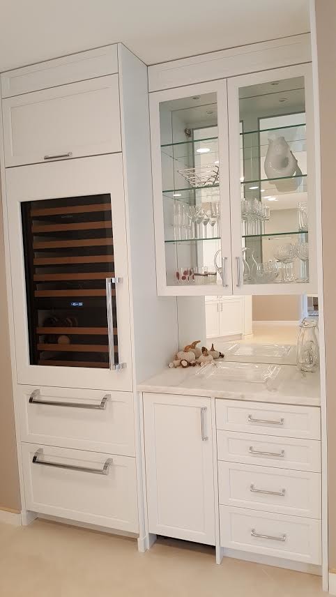 This is an example of a small transitional single-wall wet bar in San Diego with glass-front cabinets, white cabinets, marble benchtops, mirror splashback, beige floor and grey benchtop.