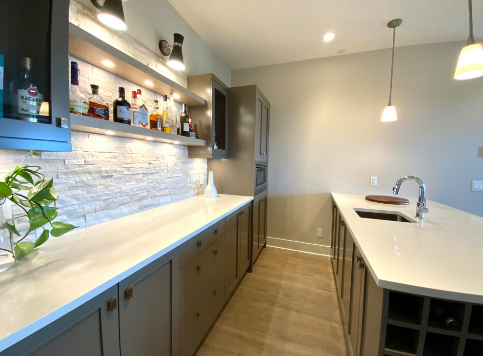 This is an example of a mid-sized transitional galley wet bar in Calgary with an undermount sink, shaker cabinets, grey cabinets, quartzite benchtops, white splashback, travertine splashback, brown floor, white benchtop and medium hardwood floors.