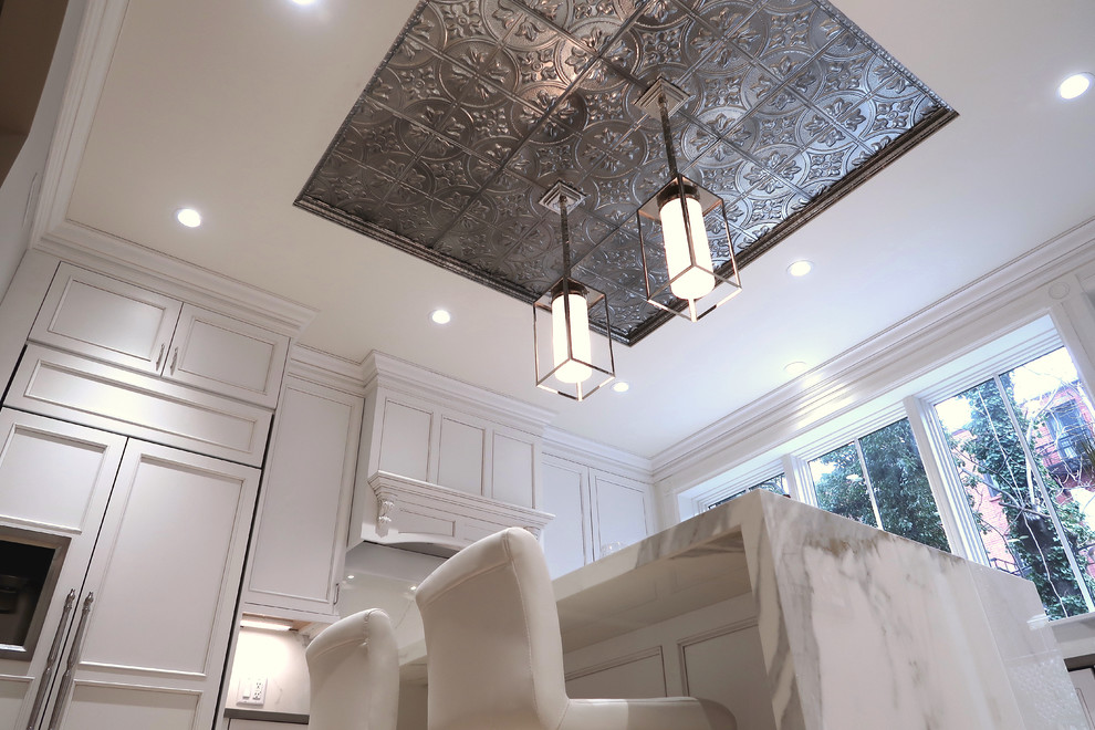 Example of a small transitional u-shaped light wood floor and brown floor enclosed kitchen design with a farmhouse sink, recessed-panel cabinets, white cabinets, quartz countertops, white backsplash, stone slab backsplash, stainless steel appliances, an island and white countertops