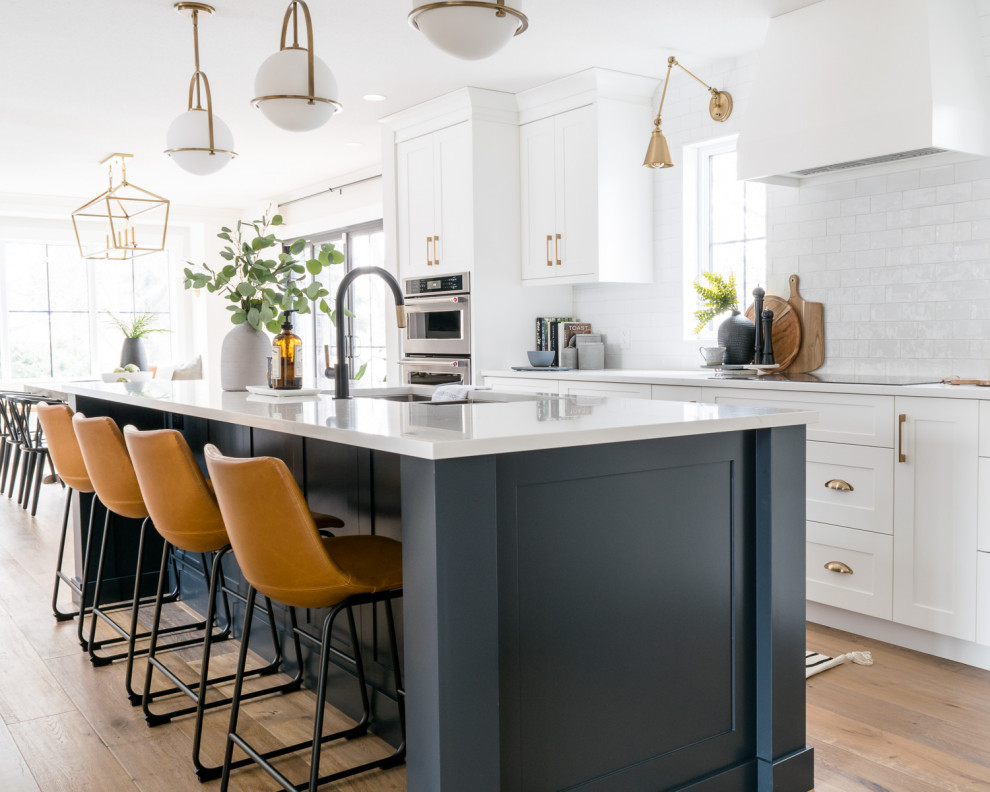 Eat-in kitchen - large transitional l-shaped medium tone wood floor and brown floor eat-in kitchen idea with a triple-bowl sink, shaker cabinets, white cabinets, quartz countertops, white backsplash, subway tile backsplash, stainless steel appliances, an island and white countertops
