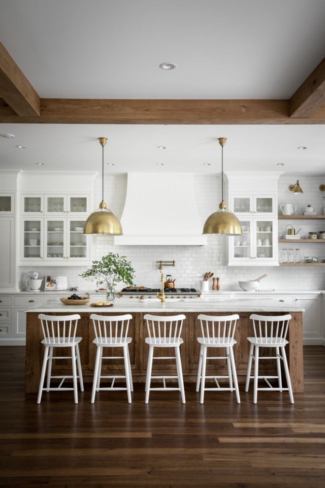 Example of a large transitional u-shaped medium tone wood floor, brown floor and exposed beam open concept kitchen design with a farmhouse sink, shaker cabinets, white cabinets, marble countertops, white backsplash, subway tile backsplash, paneled appliances, an island and white countertops